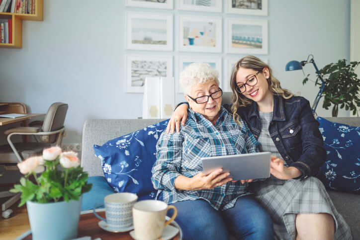 Senior caregiver assisting elderly woman with bookkeeping services on a tablet.